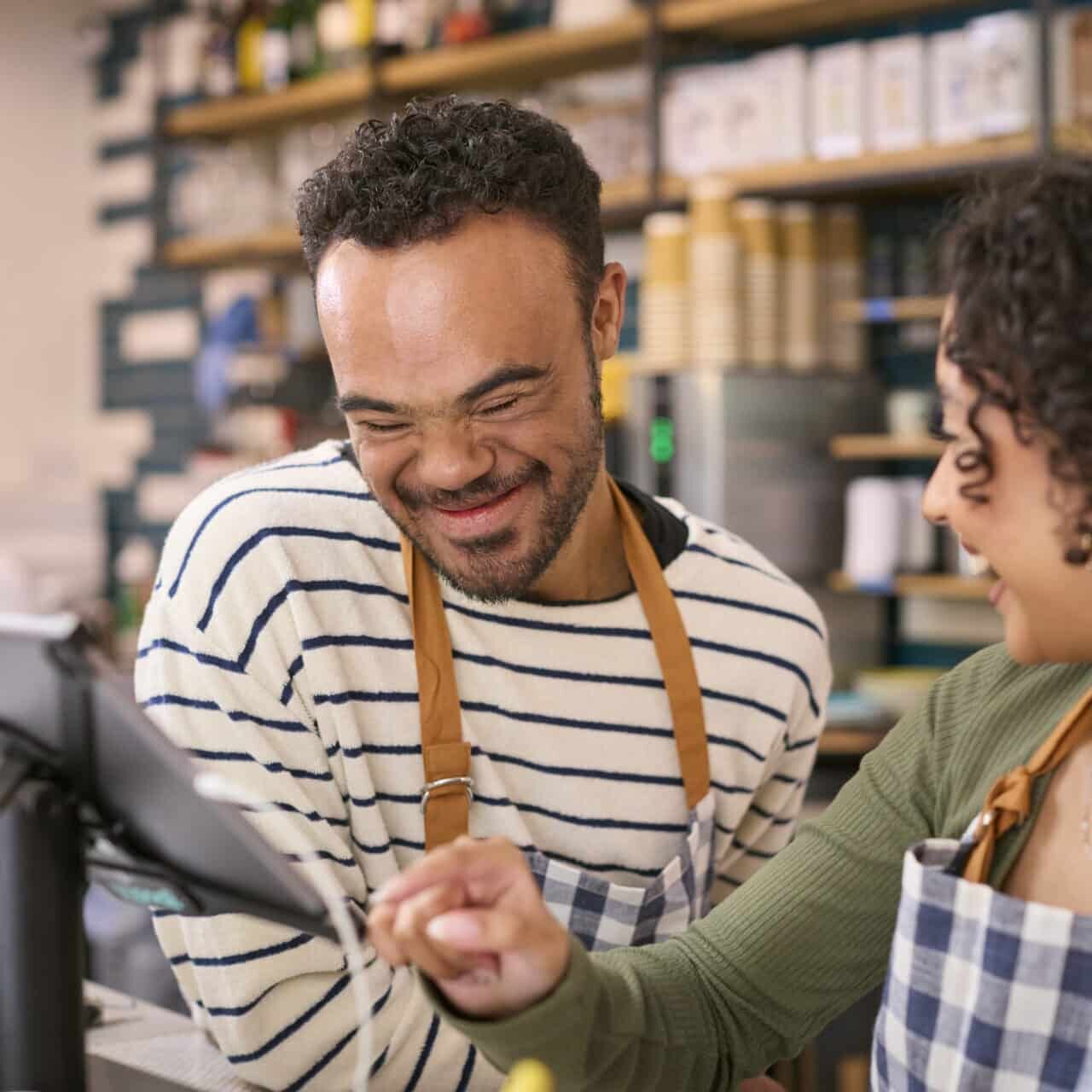 Woman Working In Food Shop Training Man How To Use Checkout